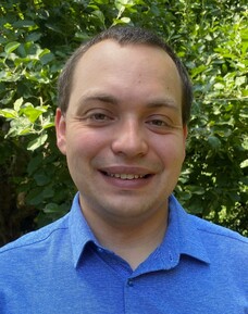 Michael Klett fröhlich lächelnd im blauen Hemd, draußen im Grünen.